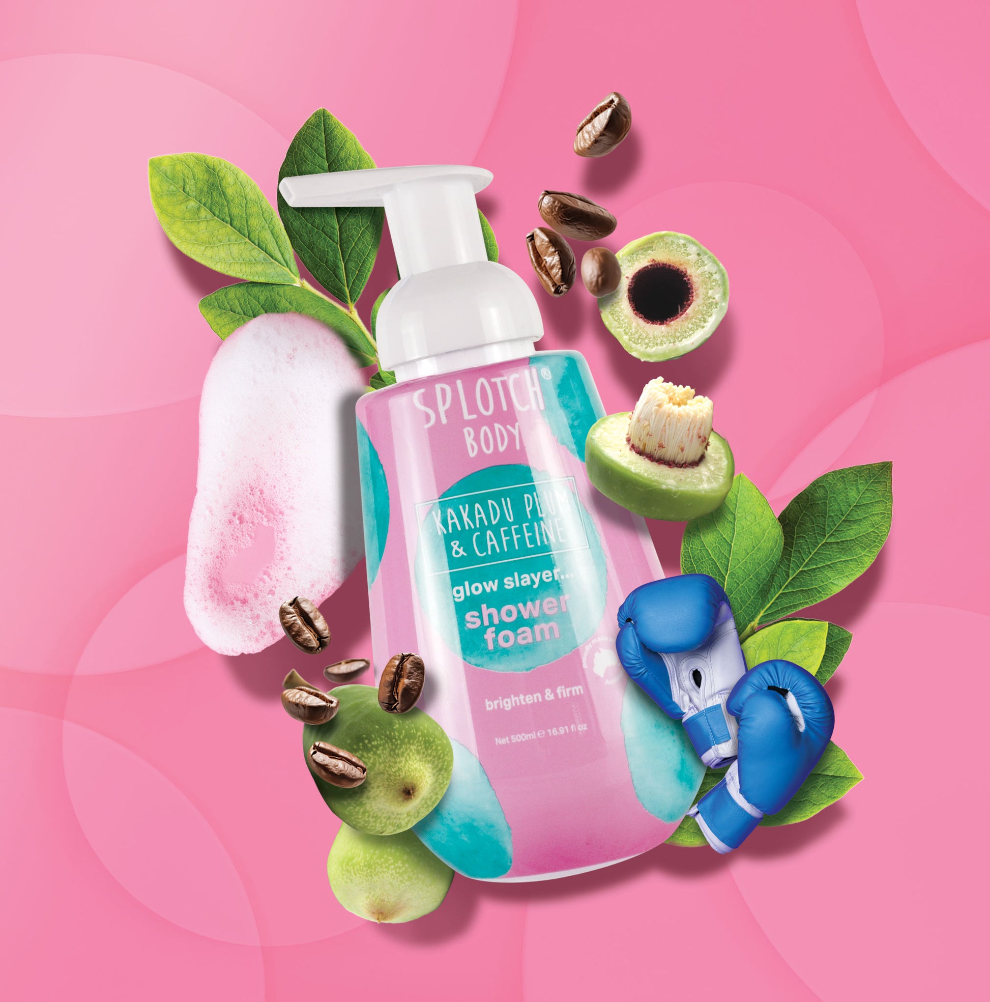 A product shot for SEO featuring a pump bottle of SPLOTCH BODY Kakadu Plum & Caffeine Shower Foam, labeled "glow slayer... shower foam" and "brighten & firm". The scene includes thick pink foam, whole and sliced Kakadu Plums, coffee beans, green leaves, and a pair of small blue boxing gloves, all resting on a pink background. The net content is 500ml 16.91fl oz.